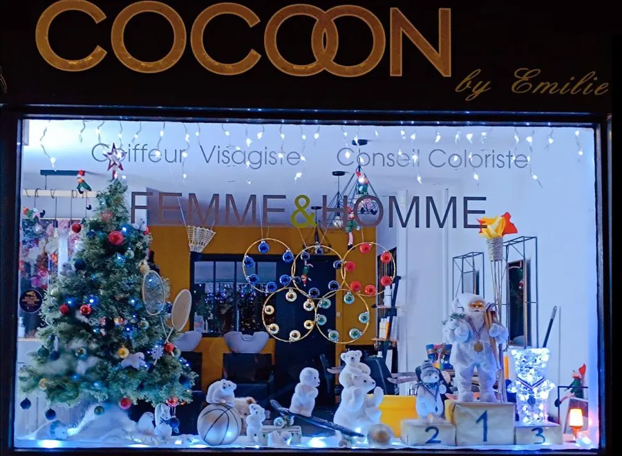 La vitrine de Noël illuminée sous l'enseigne dorée Cocoon by Emilie — salon de coiffure à Calais